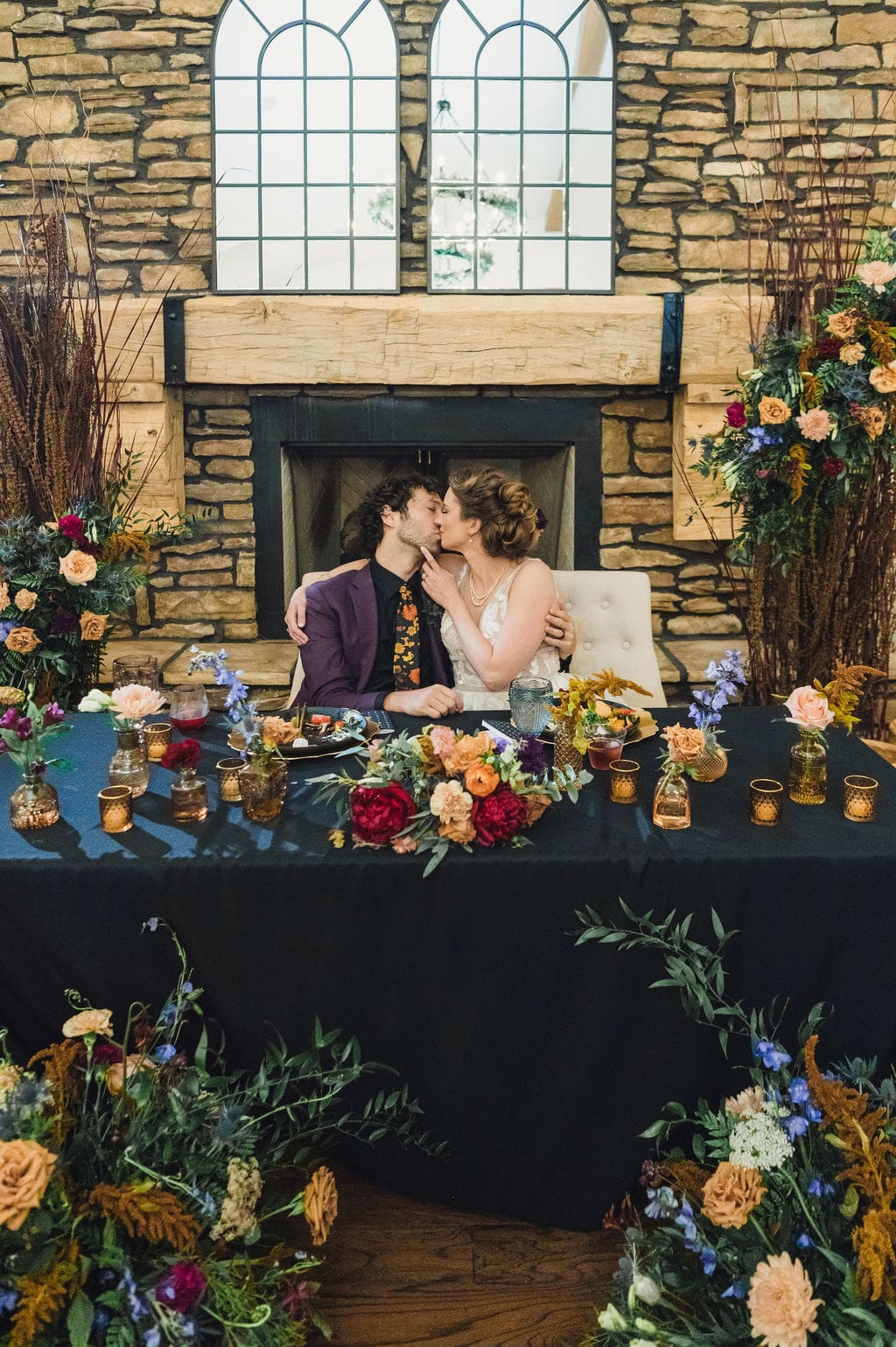 A decorated cake with floral toppers and a Love you to the moon and back sign is centered on a wooden stand, surrounded by rows of chocolate-frosted cupcakes—perfect for an Eclipse Weekend Wedding—on a black tablecloth with gold confetti.