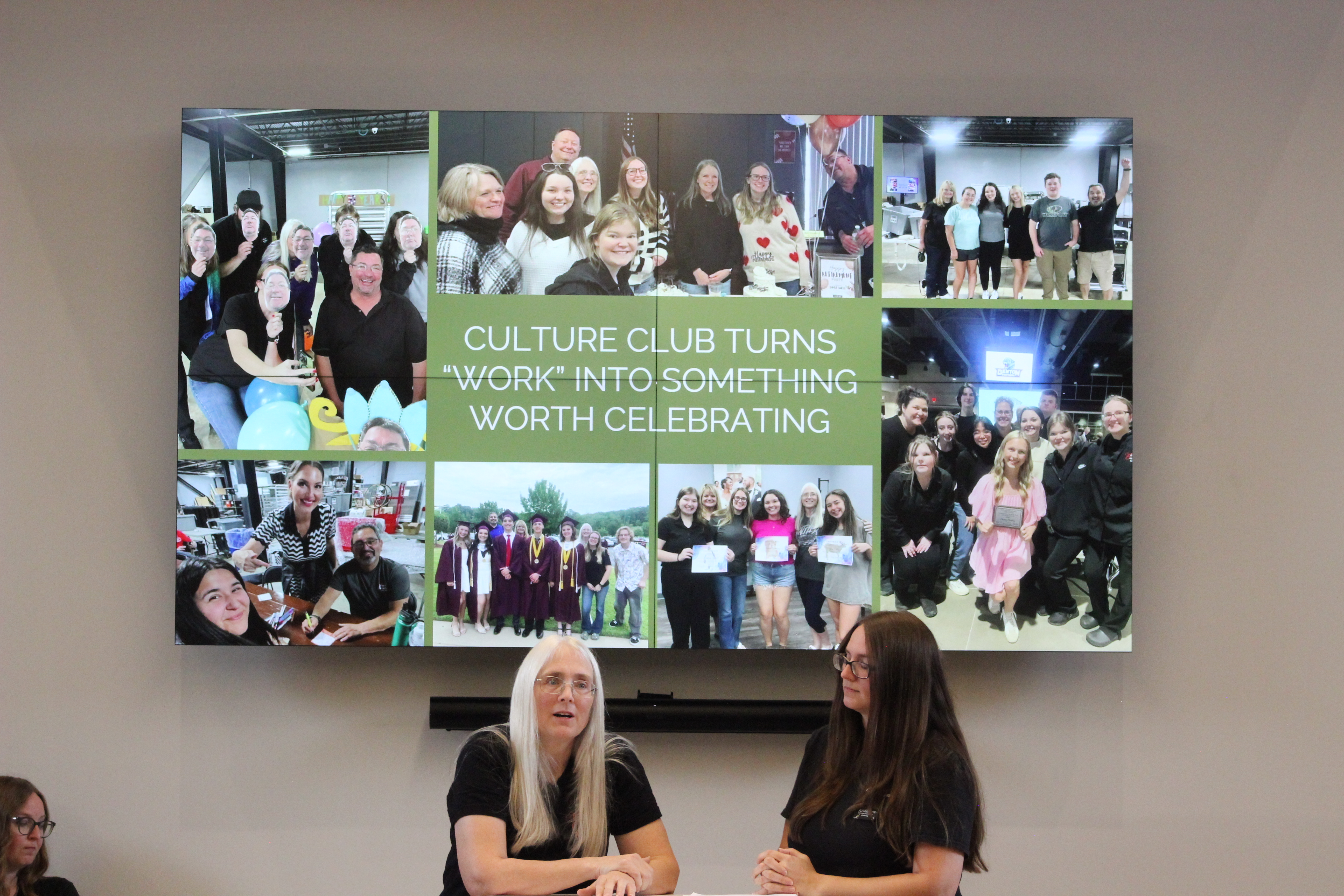 Two women sit at a table in front of a screen displaying a collage of group photos. The screen text reads, Culture Club turns work into something worth celebrating.