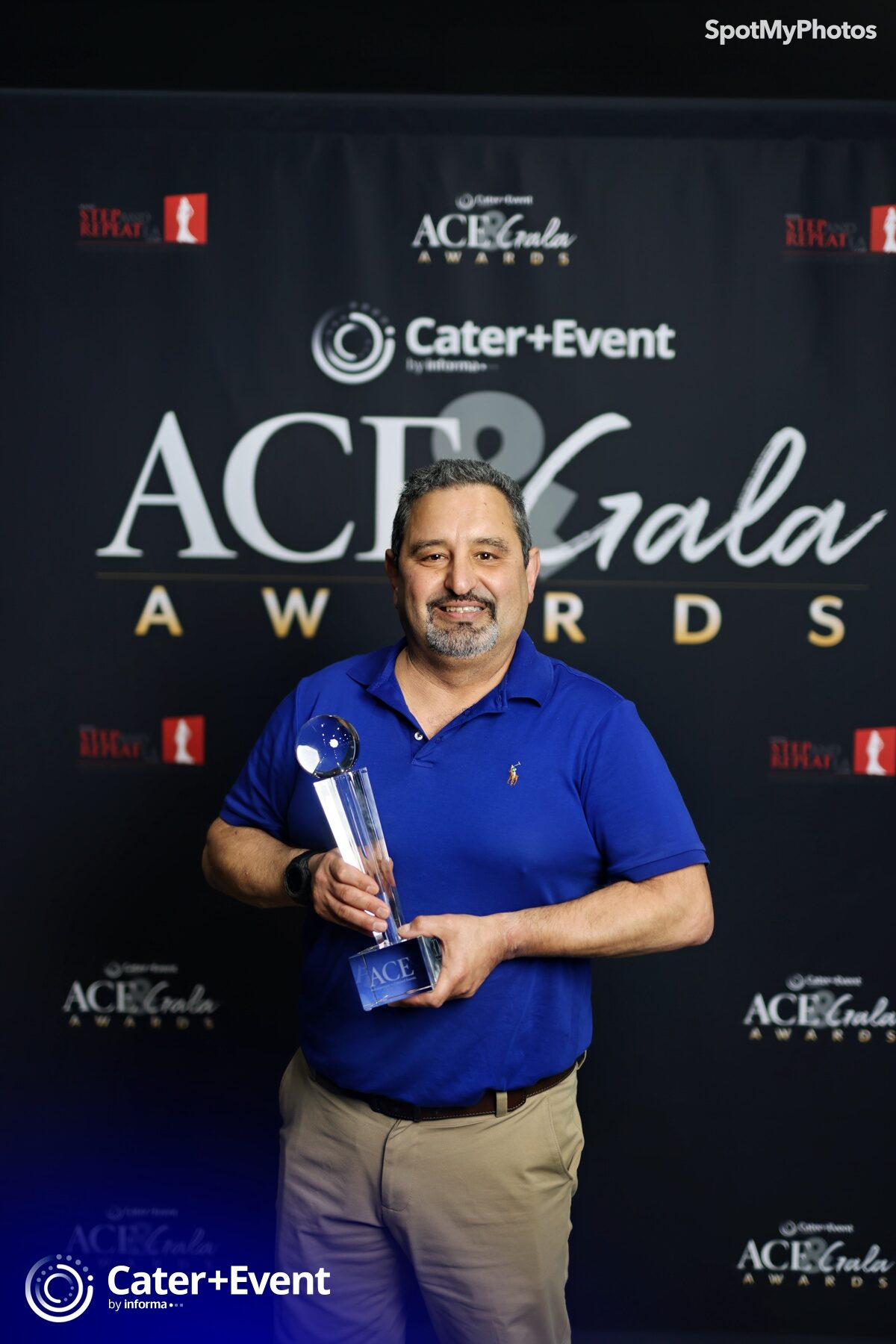 A man in a blue polo shirt smiles while holding a glass award trophy in front of a backdrop with ACE Gala Awards and Cater+Event logos.