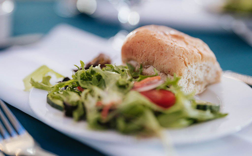 A close-up of a white plate with a fresh green salad and a bread roll, placed on a table with a blue tablecloth and silverware beside it.