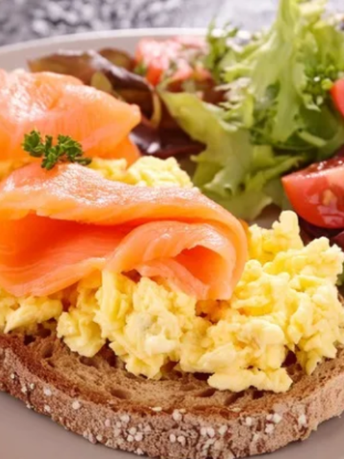 Scrambled Eggs Recipe A slice of seeded bread topped with scrambled eggs and smoked salmon, garnished with a sprig of parsley, served with a side salad of mixed greens and cherry tomatoes.