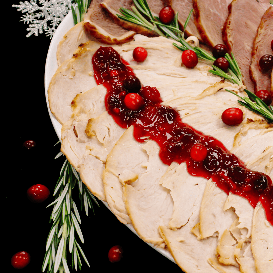 Slices of roasted turkey breast topped with cranberry sauce are arranged on a white platter, garnished with fresh rosemary sprigs and whole cranberries, with a festive snowflake decoration in the corner.