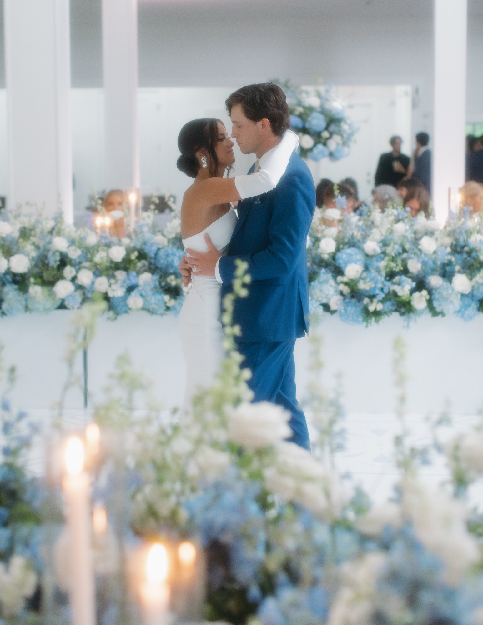 Arkansas Wedding Couple A bride and groom share a first dance in front of blue and white floral arrangements, with candles and guests visible in the background.