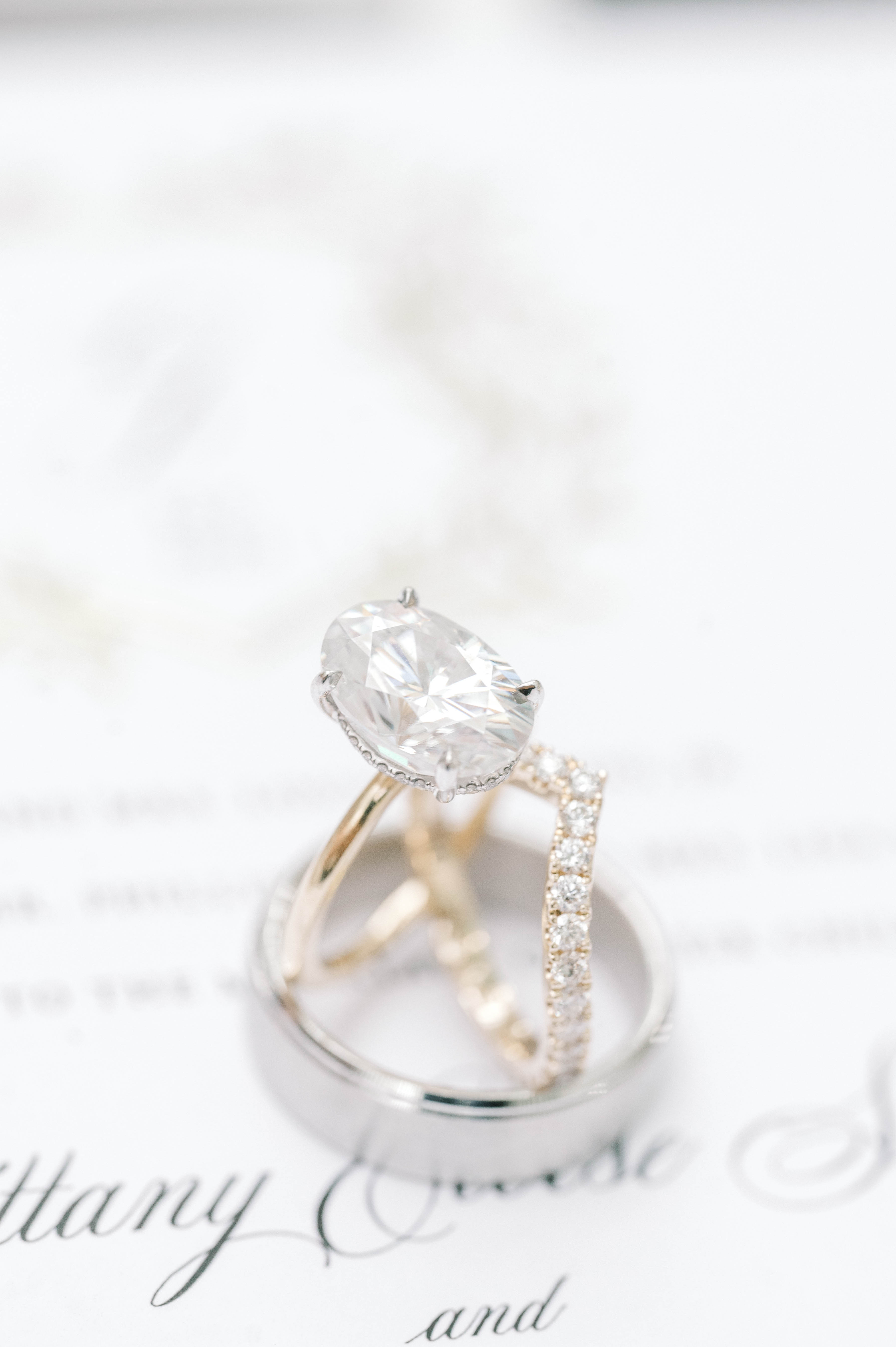 Wedding Catering Near Me A close-up of a diamond engagement ring and a diamond-studded wedding band resting on a silver ring, placed on a white printed paper background.