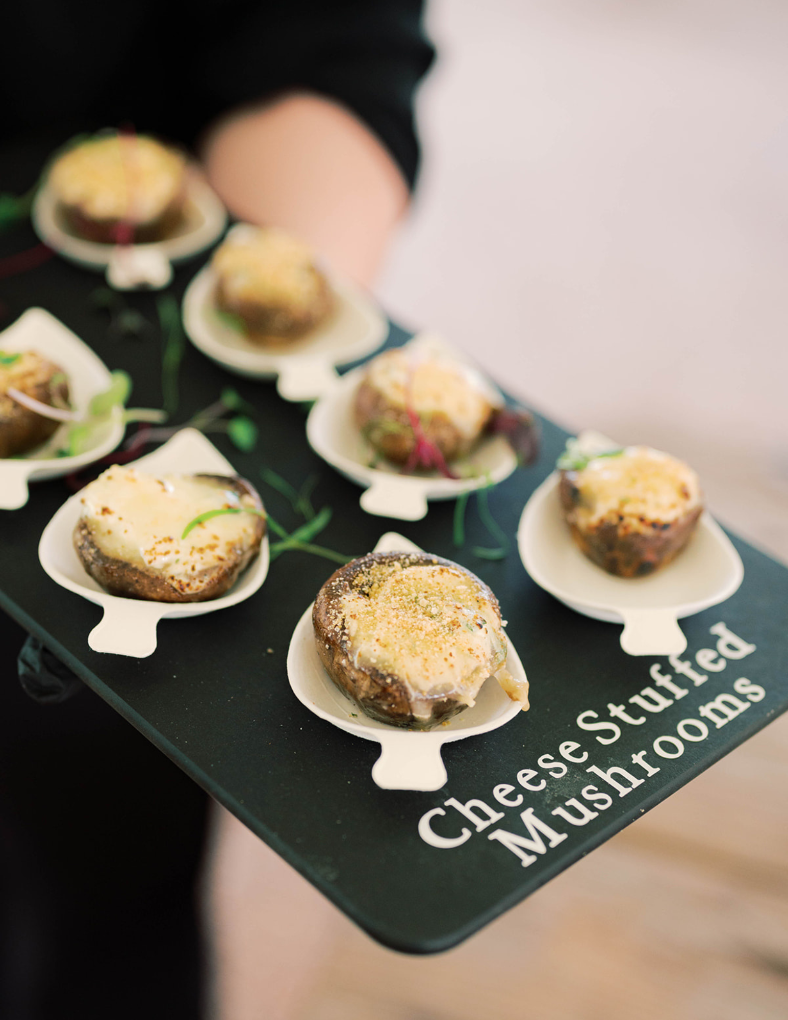 Arkansas Wedding Appetizers A person holding a tray of cheese-stuffed mushrooms, with the words Cheese Stuffed Mushrooms printed on the tray.